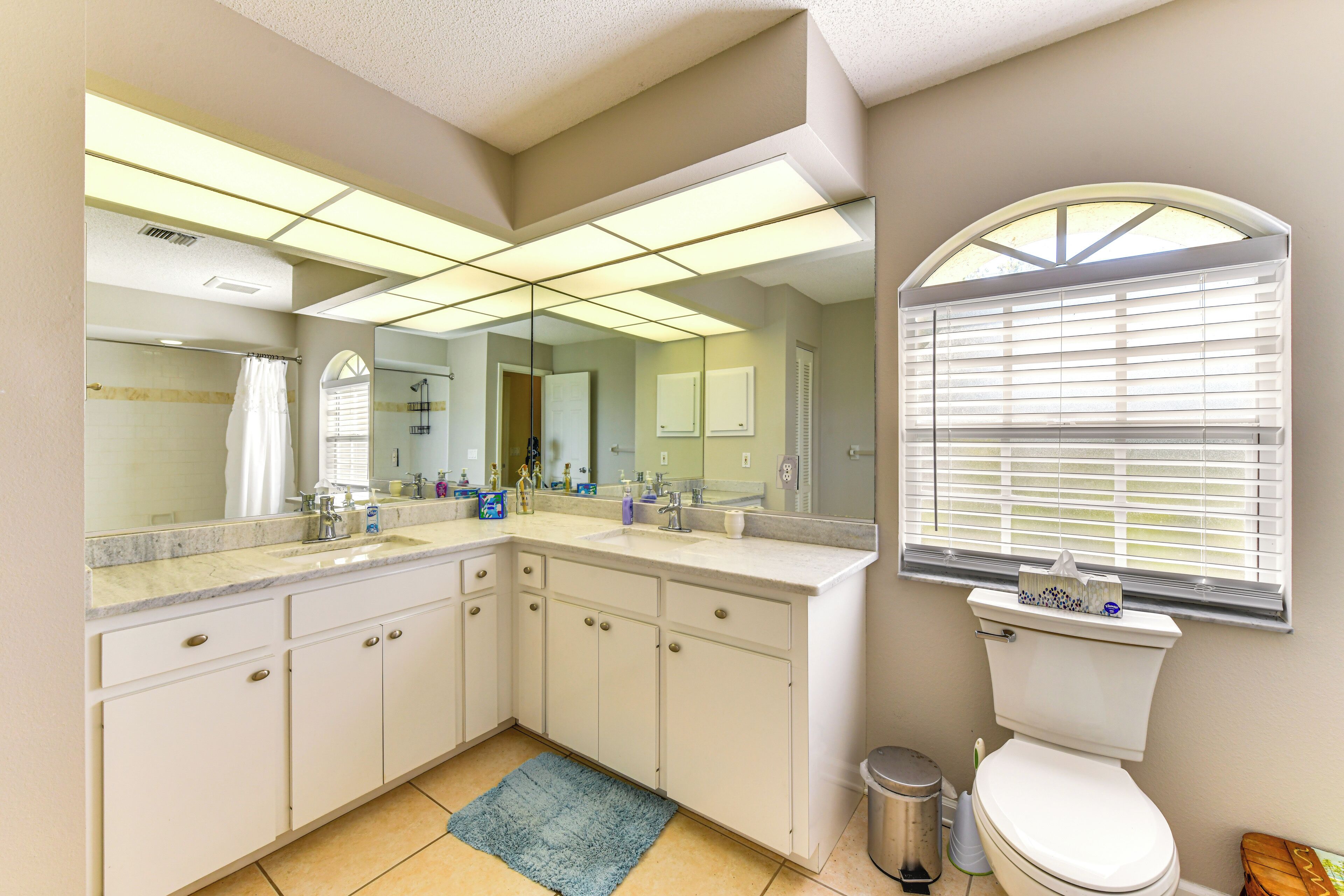A bathroom with a large mirror, a toilet, a sink, and a window with blinds.