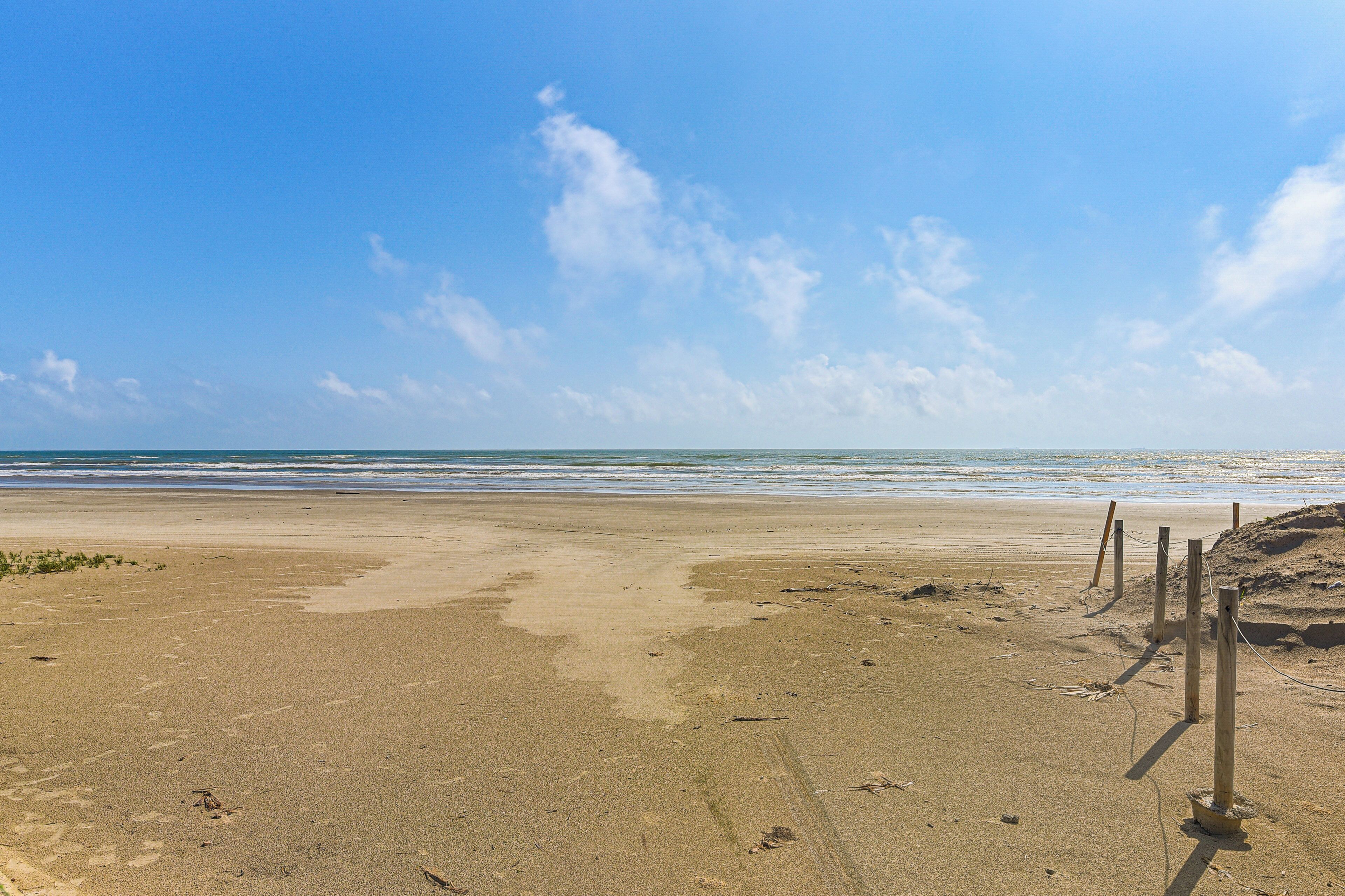 Une plage de sable fin, avec un ciel dégagé et l’océan en arrière-plan.