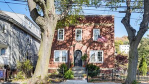 A two-story brick house with a front entrance, steps, and a small American flag. - Walk to Constitution Beach: Mid-century Boston Gem (Boston)