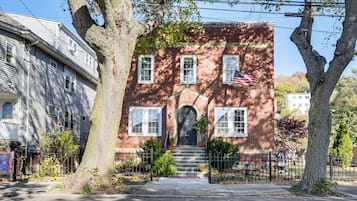 A two-story brick house with a front entrance, steps, and a small American flag.