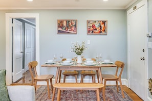 A dining area with a rectangular table set for six, surrounded by wooden chairs and benches. There are two framed artworks on the wall above the table. - Walk to Constitution Beach: Mid-century Boston Gem (Boston)