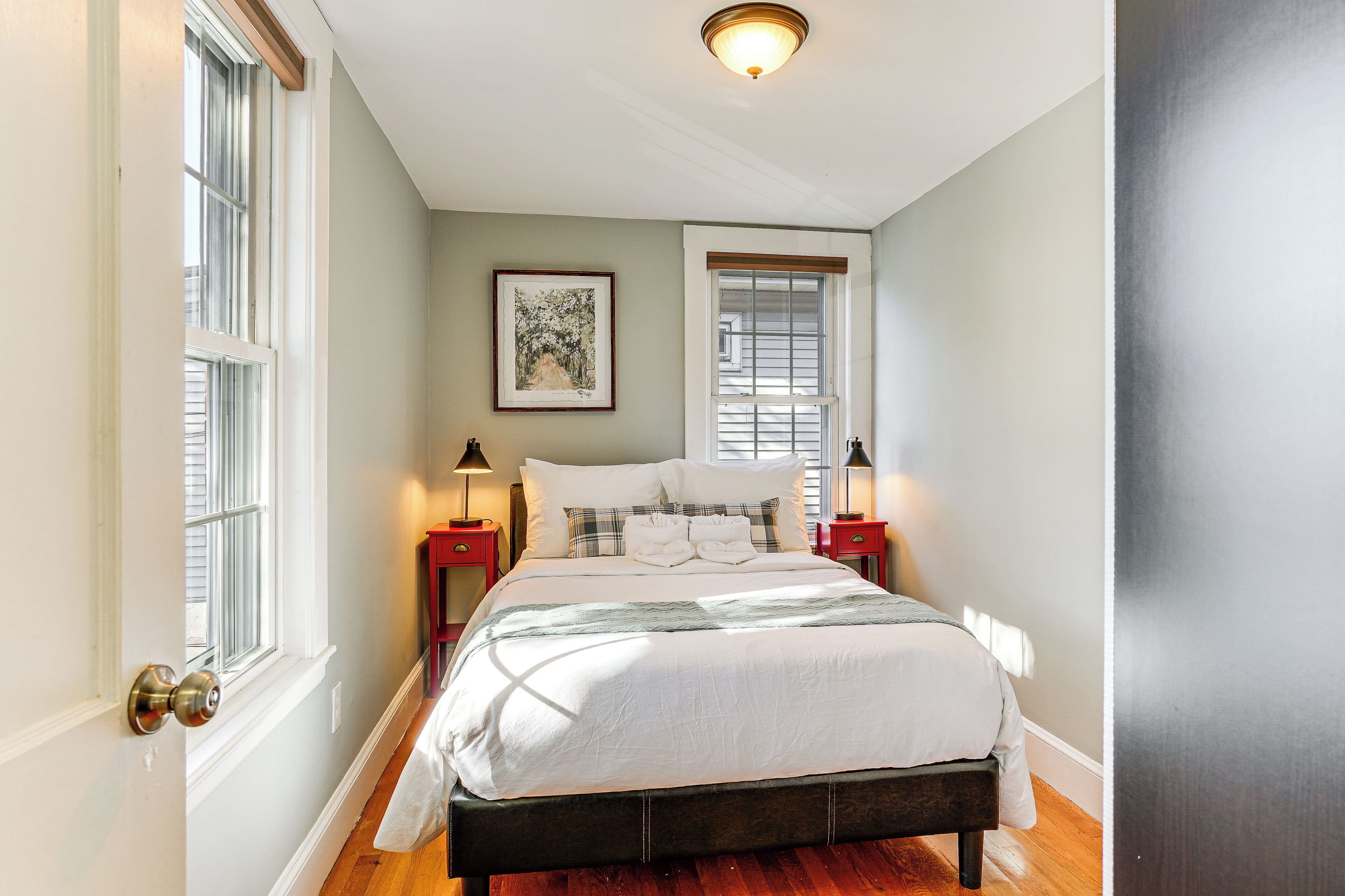 Une chambre à coucher comprenant un lit, deux tables de chevet, une fenêtre avec des stores et un luminaire au plafond.