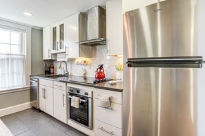 Cozinha moderna com eletrodomésticos de aço inoxidável, armários brancos e forno embutido.