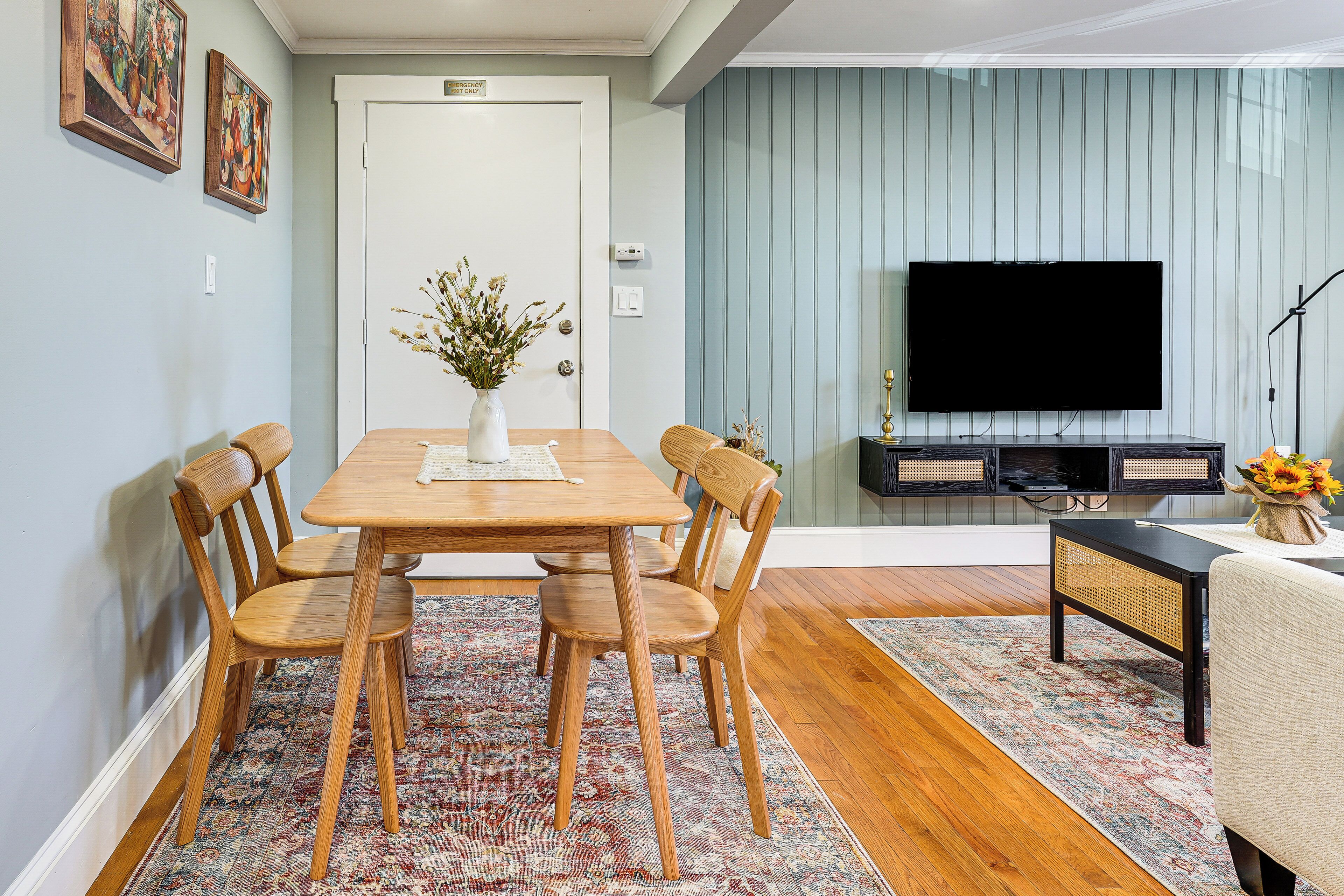 Un comedor con una mesa y sillas de madera, un florero con flores, un televisor y un sofá.