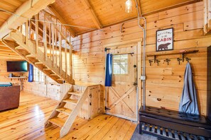 Interior de cabana com paredes de madeira, escada, um banco e um letreiro de boas-vindas.