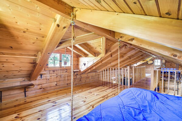 Une cabane en bois avec une chambre à coucher située en mezzanine, un plancher en bois et une bâche bleue sur le sol.