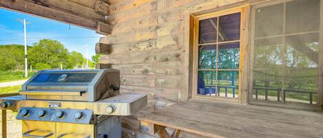 Une cabane en bois rustique, dotée d’un barbecue à gaz intégré et d’une grande fenêtre donnant sur une zone verdoyante.