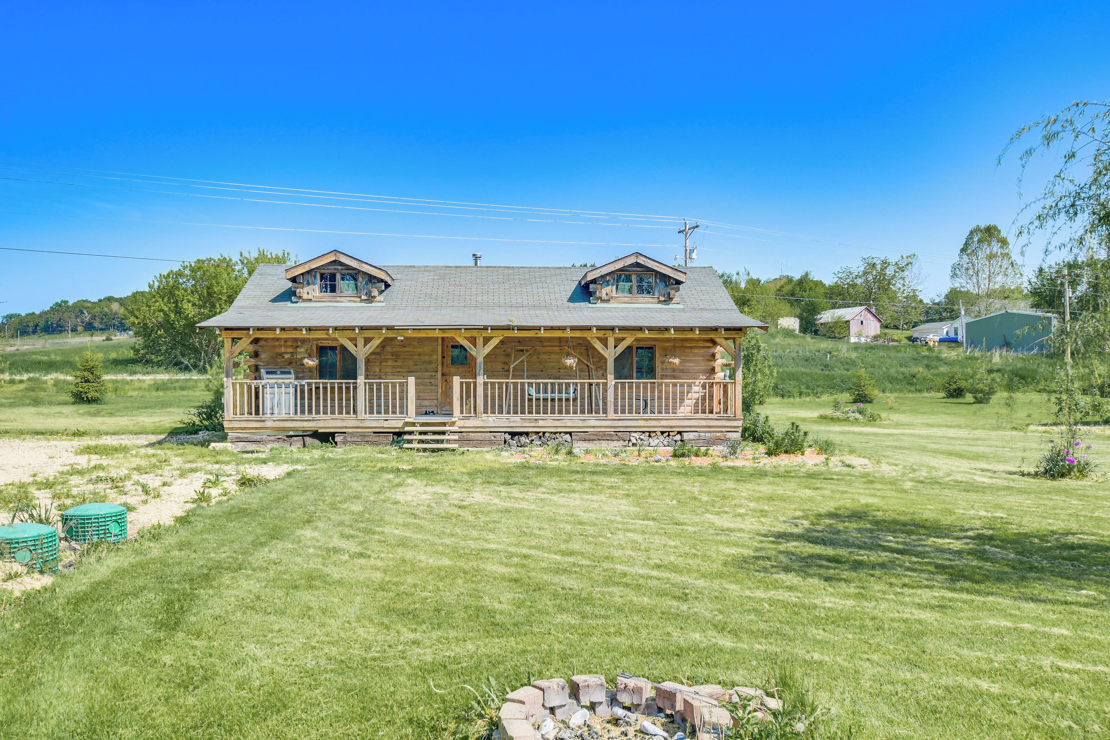 A wooden cabin with a porch, surrounded by a well-maintained lawn and a small fire pit.
