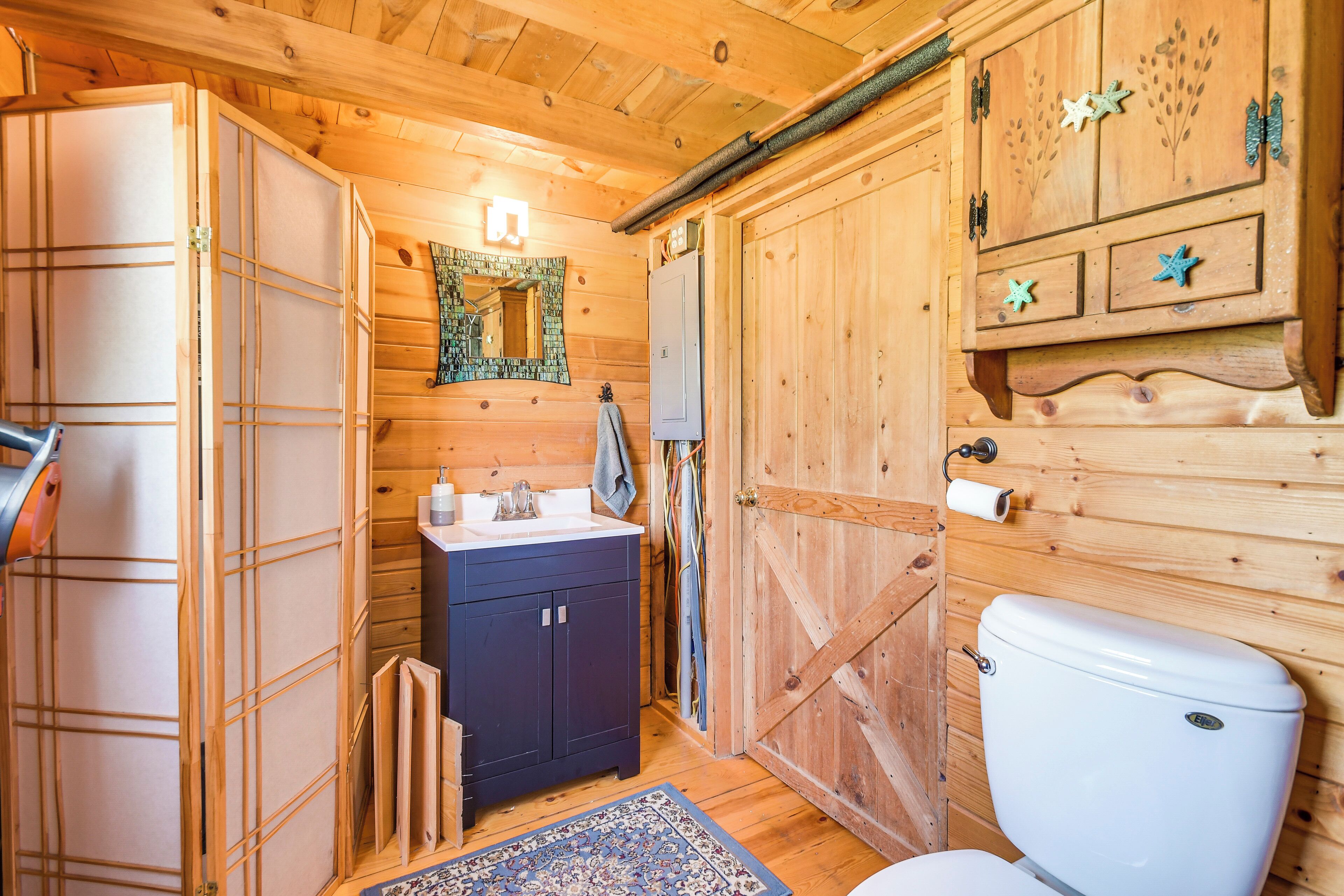 A wooden cabin bathroom with a sink, mirror, and toilet.