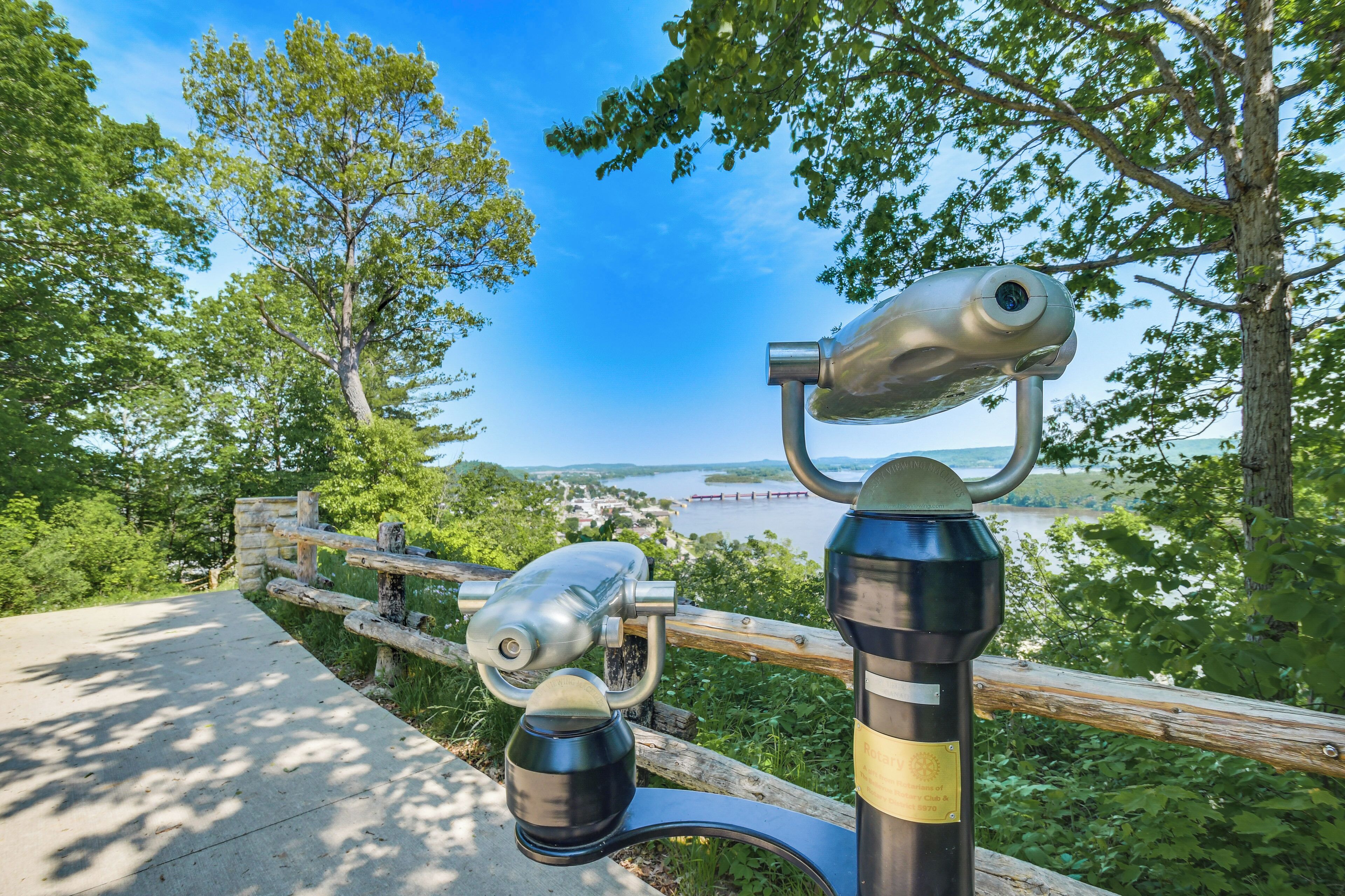 A pair of binoculars mounted on a metal stand with a wooden fence in the background.
