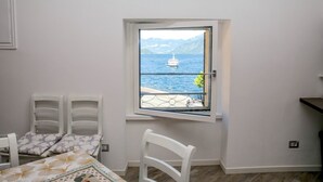 A room with a view of a body of water and mountains. There is a bed with a patterned bedspread, a chair, and a table with a tablecloth. - Casa Hygge Argegno (Argegno)