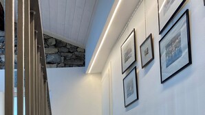 A staircase with stone steps and a wooden handrail, leading to a room with white walls and framed pictures. - Casa Hygge Argegno (Argegno)