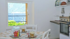 A small kitchen with a window overlooking a body of water, a table set with cups and jars, and a microwave on the counter. - Casa Hygge Argegno (Argegno)