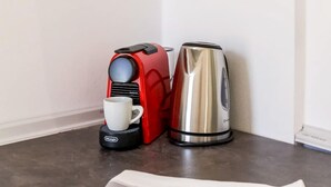 Un coin cuisine équipé d’une machine à café, d’une bouilloire et d’un journal posé sur le comptoir.