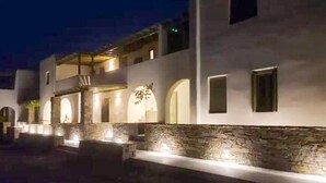 A modern building with a stone facade, arched windows, and a well-lit entrance. - Ampelas Nostalgia Apartments - Aiolos Gem in Paros (Paros)