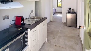 A modern kitchen with a built-in oven, a microwave, and a coffee machine. There is a window providing natural light and a view of the outside. - Ampelas Nostalgia Apartments - Aiolos Gem in Paros (Paros)