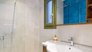 Casa de banho moderna com cabine de chuveiro em vidro, lavatório branco com toucador de madeira e espelho com moldura verde.