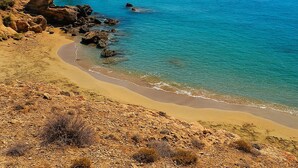 A coastal landscape with a sandy beach, rocky outcrops, and clear blue sea under a clear sky.