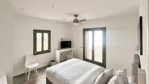 A bedroom with a bed, a desk, a chair, a TV, and two windows. - Ampelas Nostalgia Gem - Seaview Getaway in Paros (Paros)
