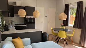 A modern kitchen with black cabinets, a built-in oven, and a dining area with yellow chairs and a round table. - Modern Chalet With Garden, Terrace (Sint Maartensvlotbrug)