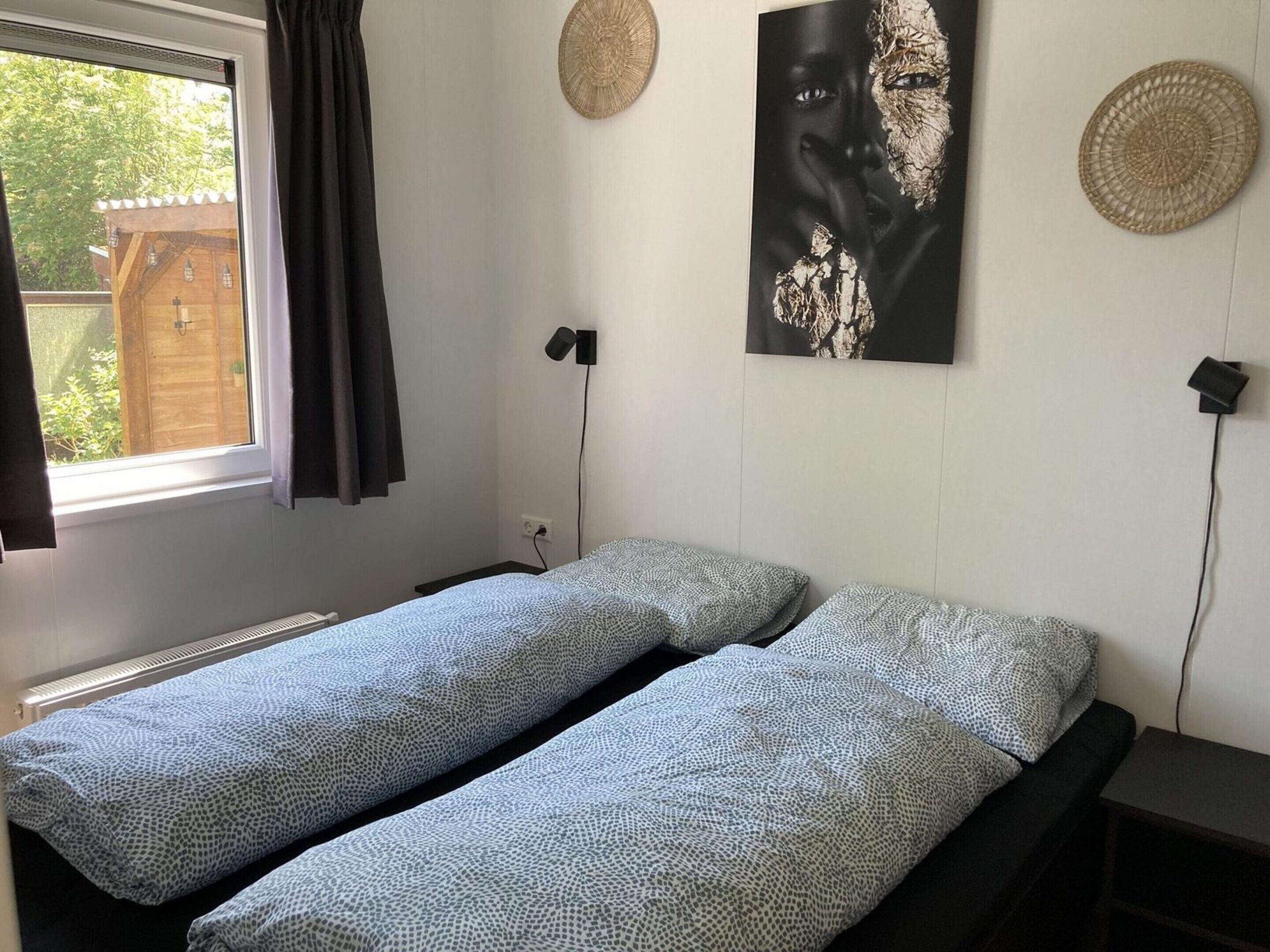 A bedroom with two beds, a window with curtains, a wall-mounted lamp, and a wall decoration.
