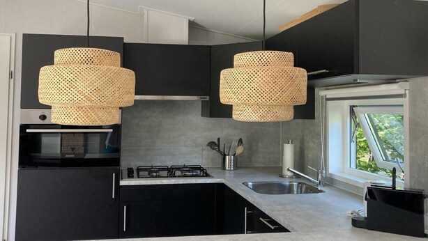 A modern kitchen with black cabinets, a gas stove, a sink, and two woven pendant lights. - Modern Chalet With Garden, Terrace (Sint Maartensvlotbrug)