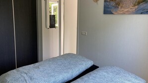 A bedroom with a bed, a door, and a wall-mounted painting. - Modern Chalet With Garden, Terrace (Sint Maartensvlotbrug)