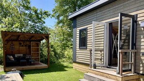 A wooden cabin with a covered outdoor seating area, a patio with a table and chairs, and a large window. - Modern Chalet With Garden, Terrace (Sint Maartensvlotbrug)