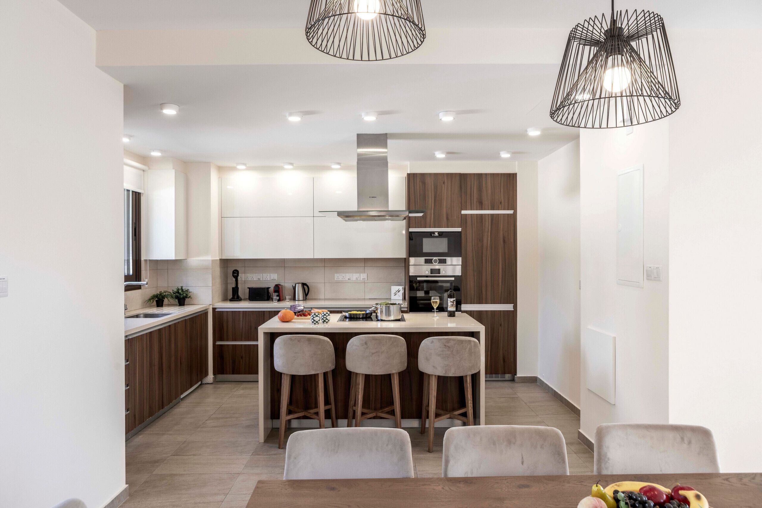 A modern kitchen with a central island, bar stools, and pendant lighting.