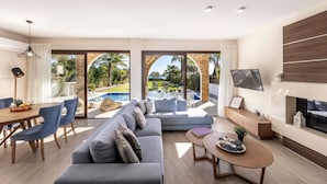 Ein modernes Wohnzimmer mit Blick auf einen Pool, eine Couch, ein Esstisch und ein Fernseher.
