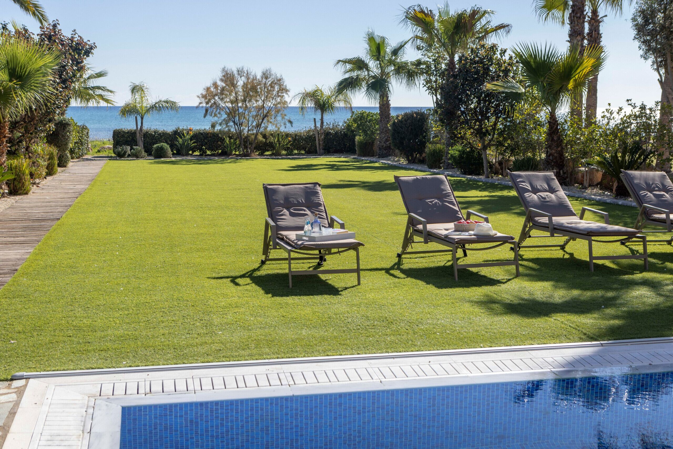 A poolside area with lounge chairs, a well-maintained lawn, and a view of the sea.