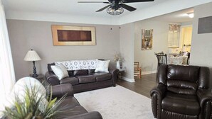 A living room with a dark brown leather sofa, a matching armchair, a ceiling fan, and a dining area in the background. - Charming 2-bedroom apartment with AC, WIFI, Security Cameras at entrances. (Windsor)