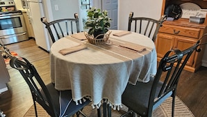 A dining area with a round table, four chairs, a central plant, and a wooden cabinet in the background. - Charming 2-bedroom apartment with AC, WIFI, Security Cameras at entrances. (Windsor)