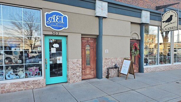 A storefront with a blue sign reading "AEI Studio & Gifts" and a blackbird sign for "Blackbirds." - Charming 2-bedroom apartment with AC, WIFI, Security Cameras at entrances. (Windsor)