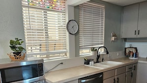 A kitchen with a microwave, sink, and cabinets. There is a clock on the wall and a plant on the counter. - Charming 2-bedroom apartment with AC, WIFI, Security Cameras at entrances. (Windsor)