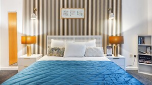 A neatly arranged hotel room with a bed, two bedside lamps, a nightstand, a bookshelf, and a wall-mounted picture frame. - Grain Store One Bed Luxury Property  (London)