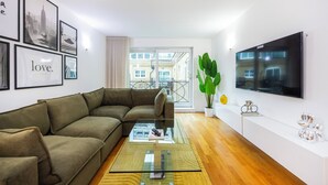 A modern living room with a sectional sofa, a glass coffee table, and a large TV mounted on the wall. - Grain Store One Bed Luxury Property  (London)