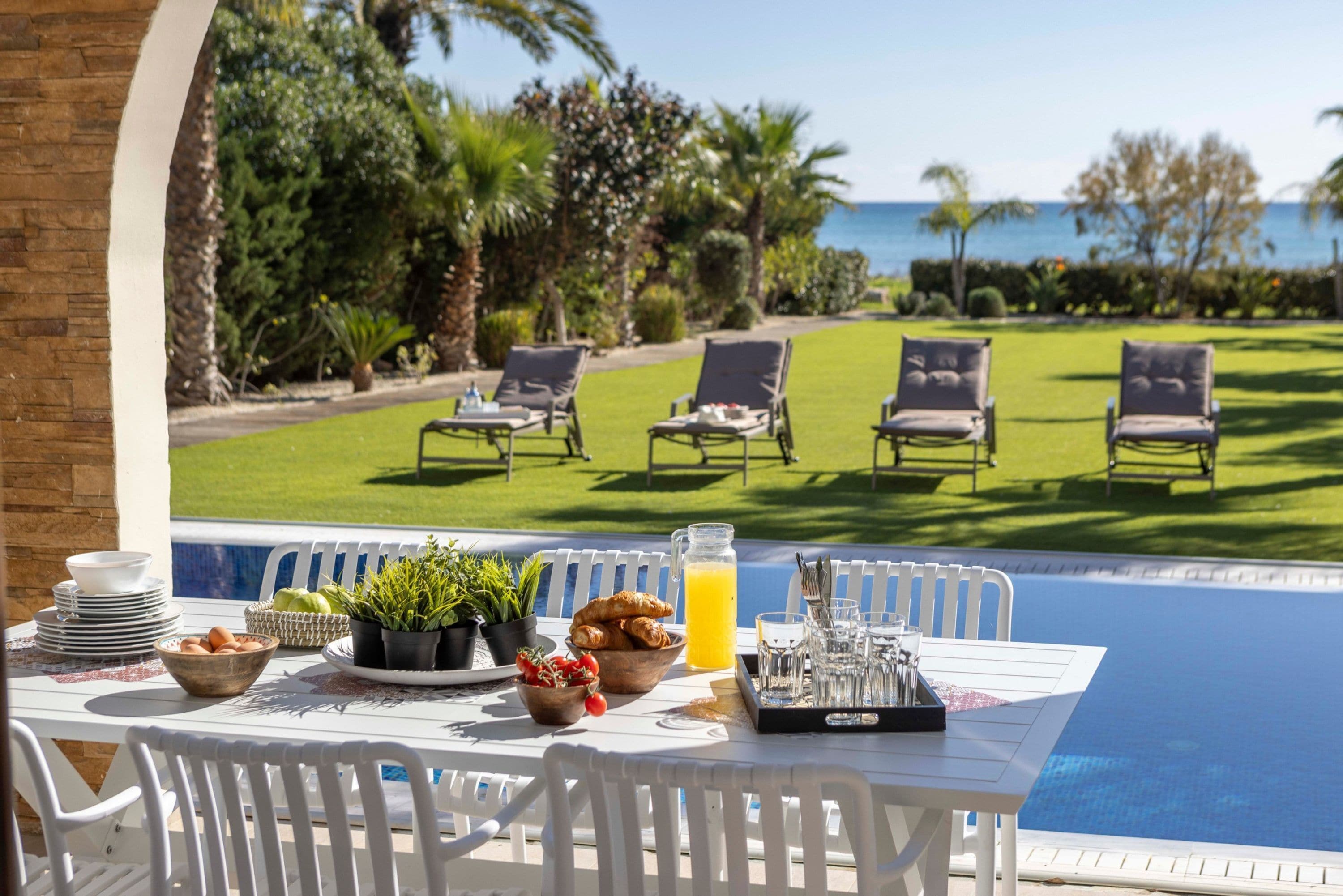 A poolside table with breakfast items, a view of the pool, and lounge chairs.