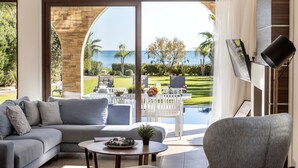A modern living room with a sofa, coffee table, and a view of a pool and outdoor seating area. - Ayia Napa Seafront Ionion Villa H5 (Sotira)