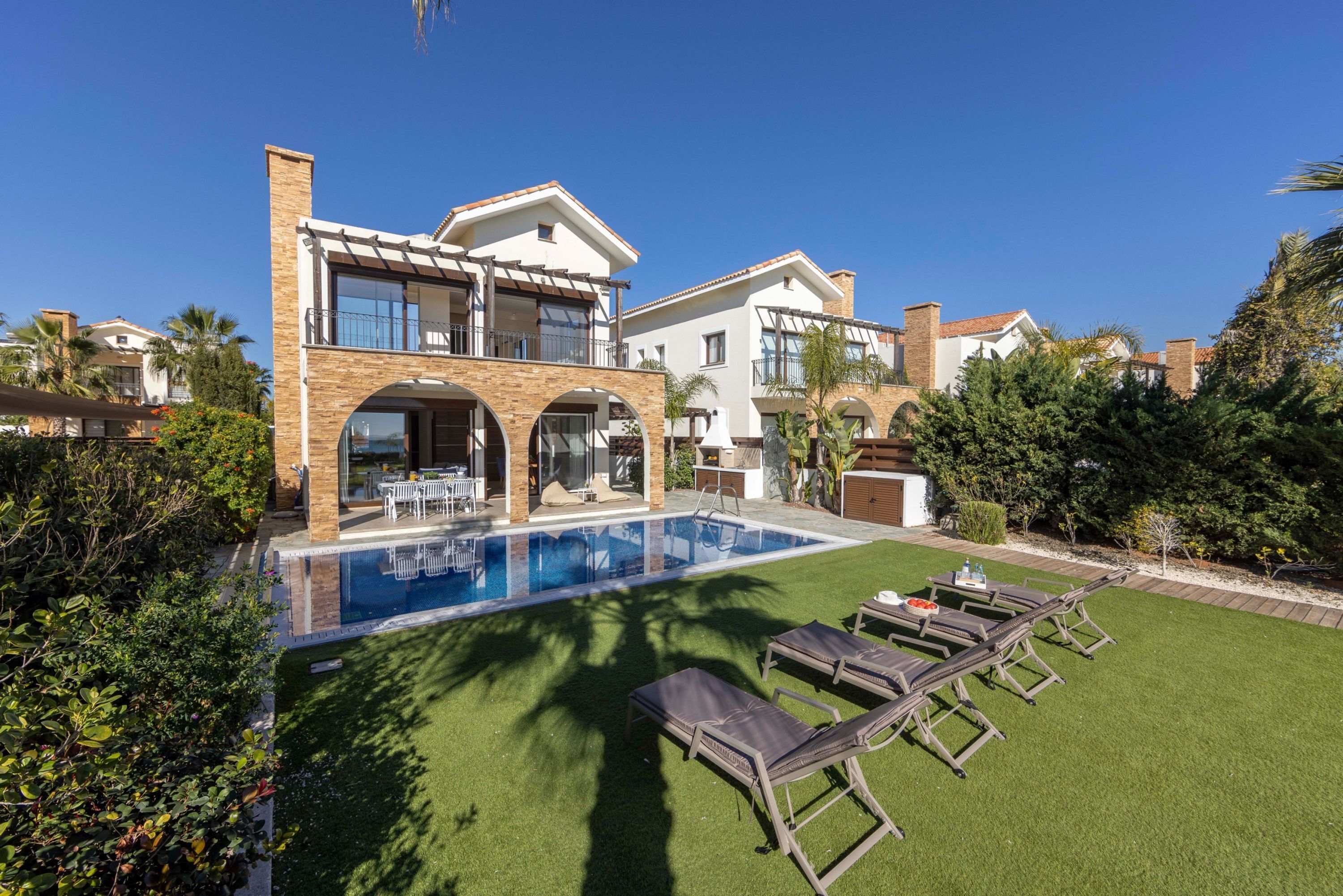 A two-story house with a swimming pool, outdoor seating, and a well-maintained lawn.