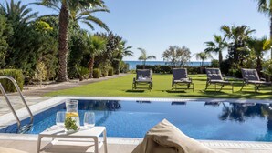 A pool with lounge chairs, a table with a pitcher and glasses, and a view of the sea. - Ayia Napa Seafront Ionion Villa H5 (Sotira)