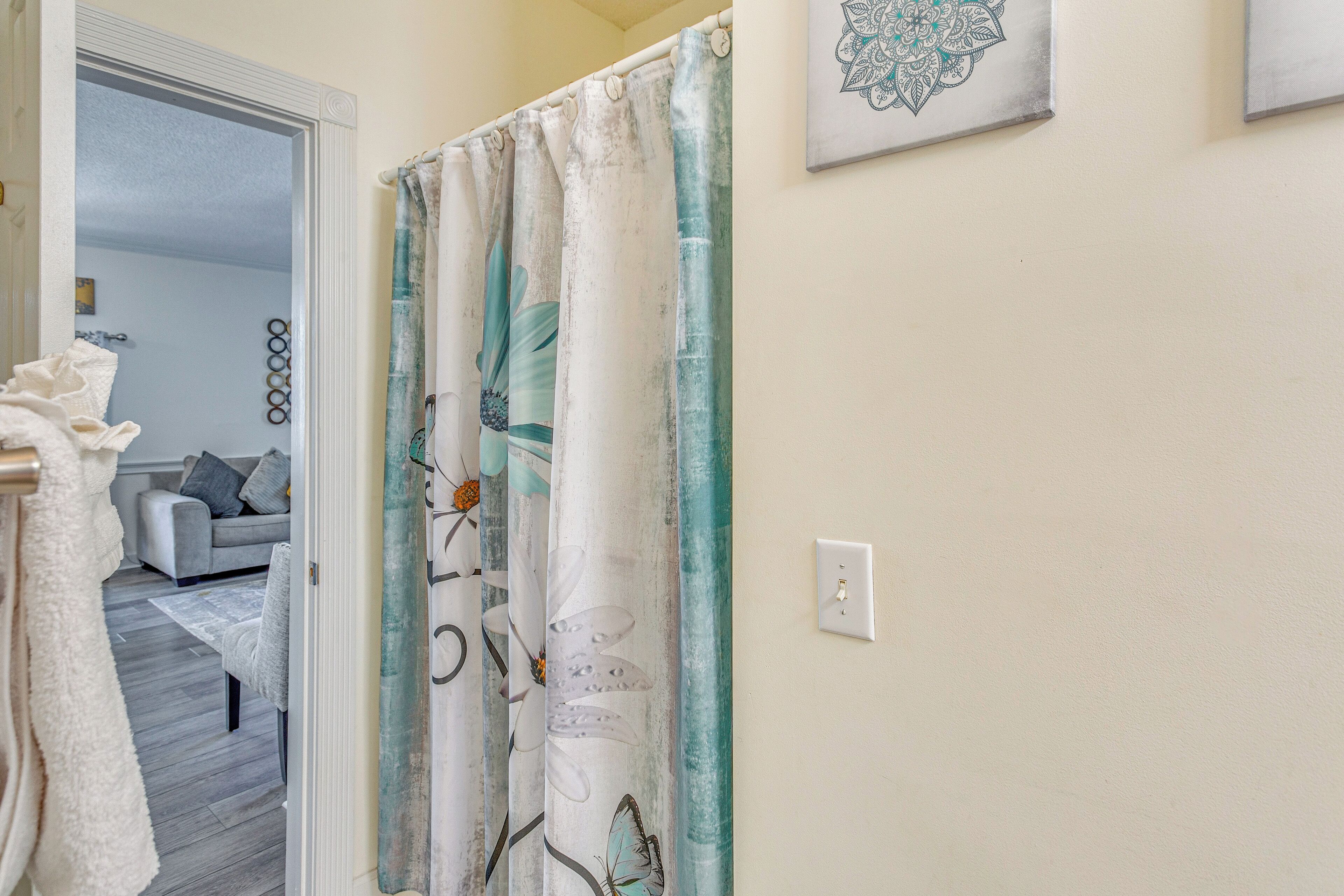 A bathroom with a shower curtain featuring floral and butterfly designs, a white towel hanging on the door, and a light switch on the wall.