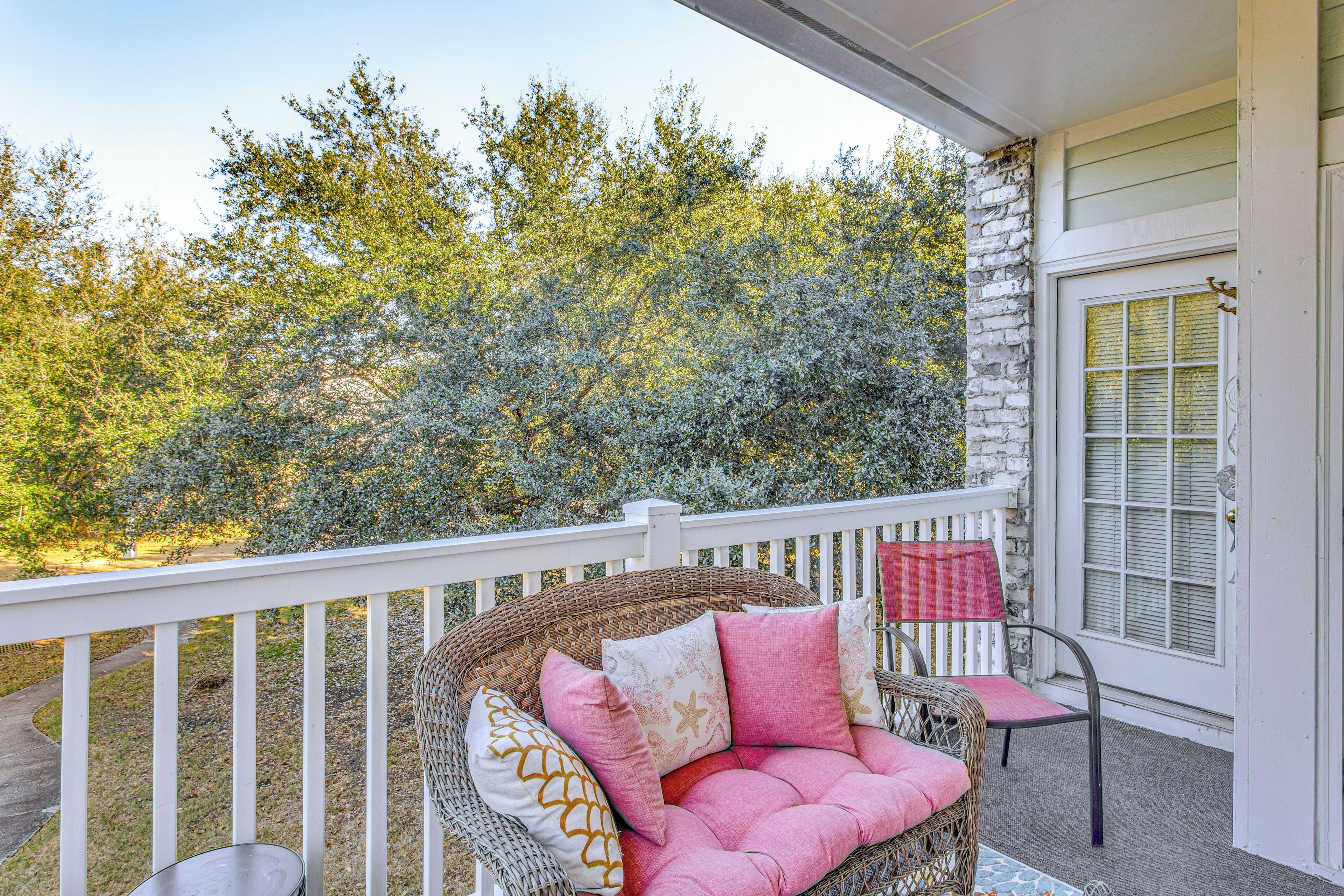 A wicker chair with pink cushions on a balcony with a white railing.