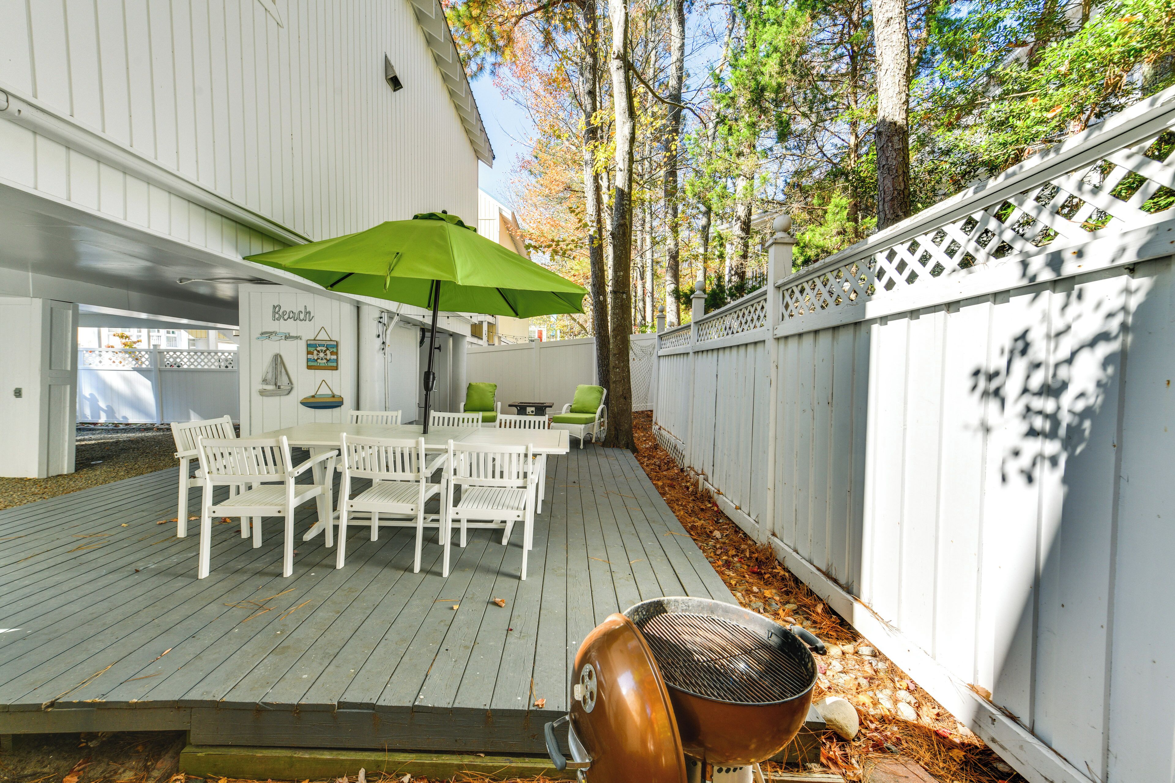 Eine Terrasse im Freien mit Grill, weißer Möbel und einem grünen Sonnenschirm.