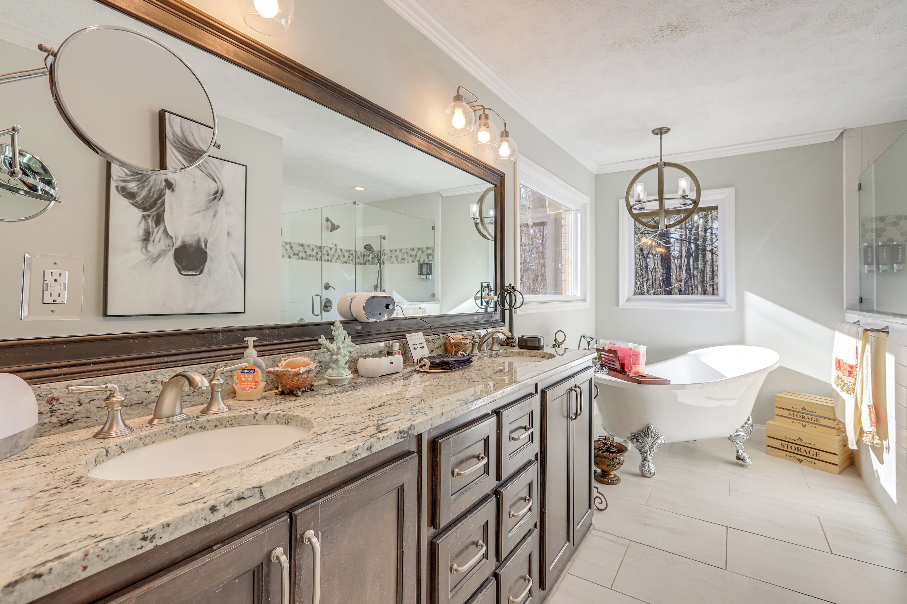 A bathroom with a large mirror, a bathtub, and a vanity with a sink and multiple drawers.