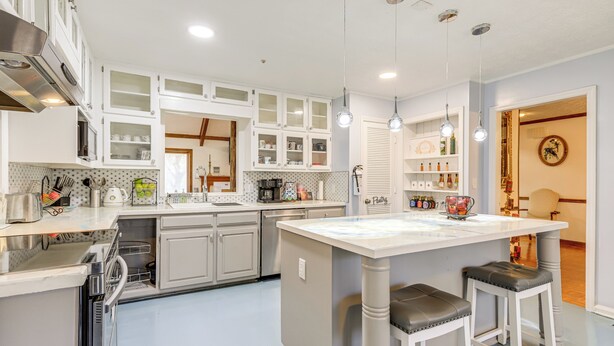 Une cuisine moderne avec des meubles blancs, un îlot central et des luminaires suspendus.