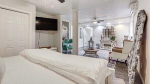 Une chambre dotée d’un grand lit, d’un ventilateur de plafond, d’une télévision et offrant une vue sur un espace de vie comprenant un canapé et une table basse.