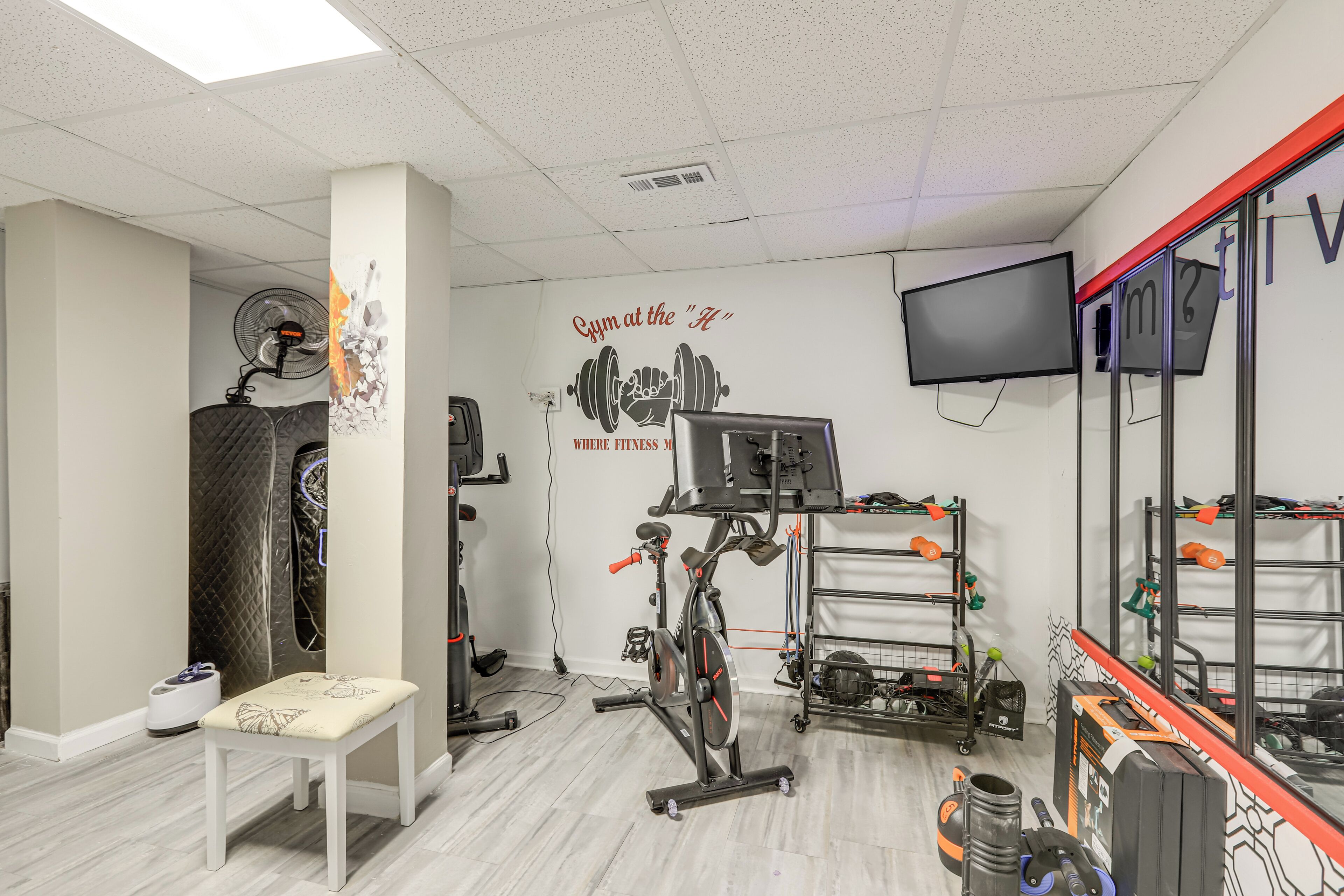 A gym with a wall-mounted TV, exercise equipment, and a bench.