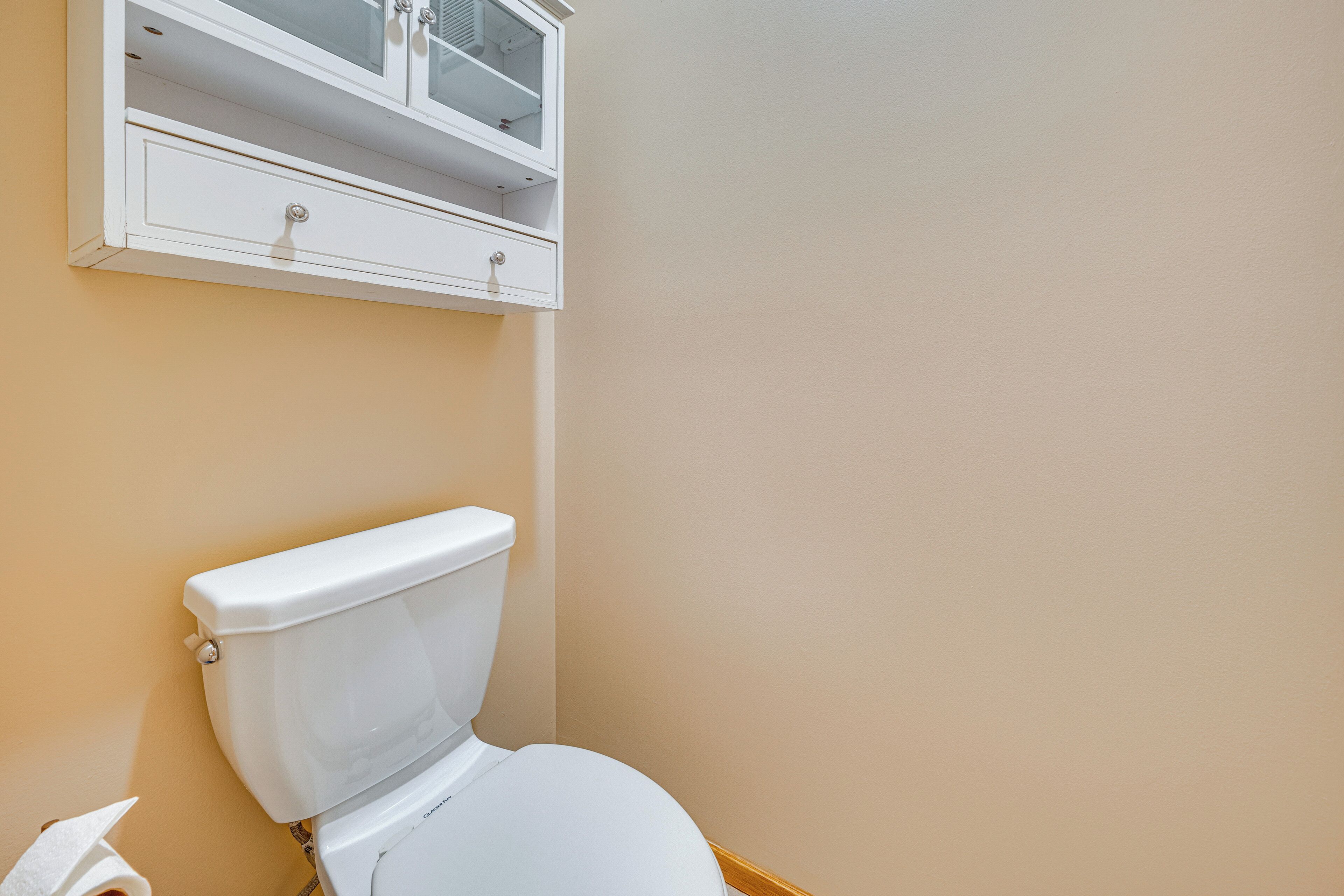 A bathroom with a toilet, a cabinet above it, and a towel on the floor.