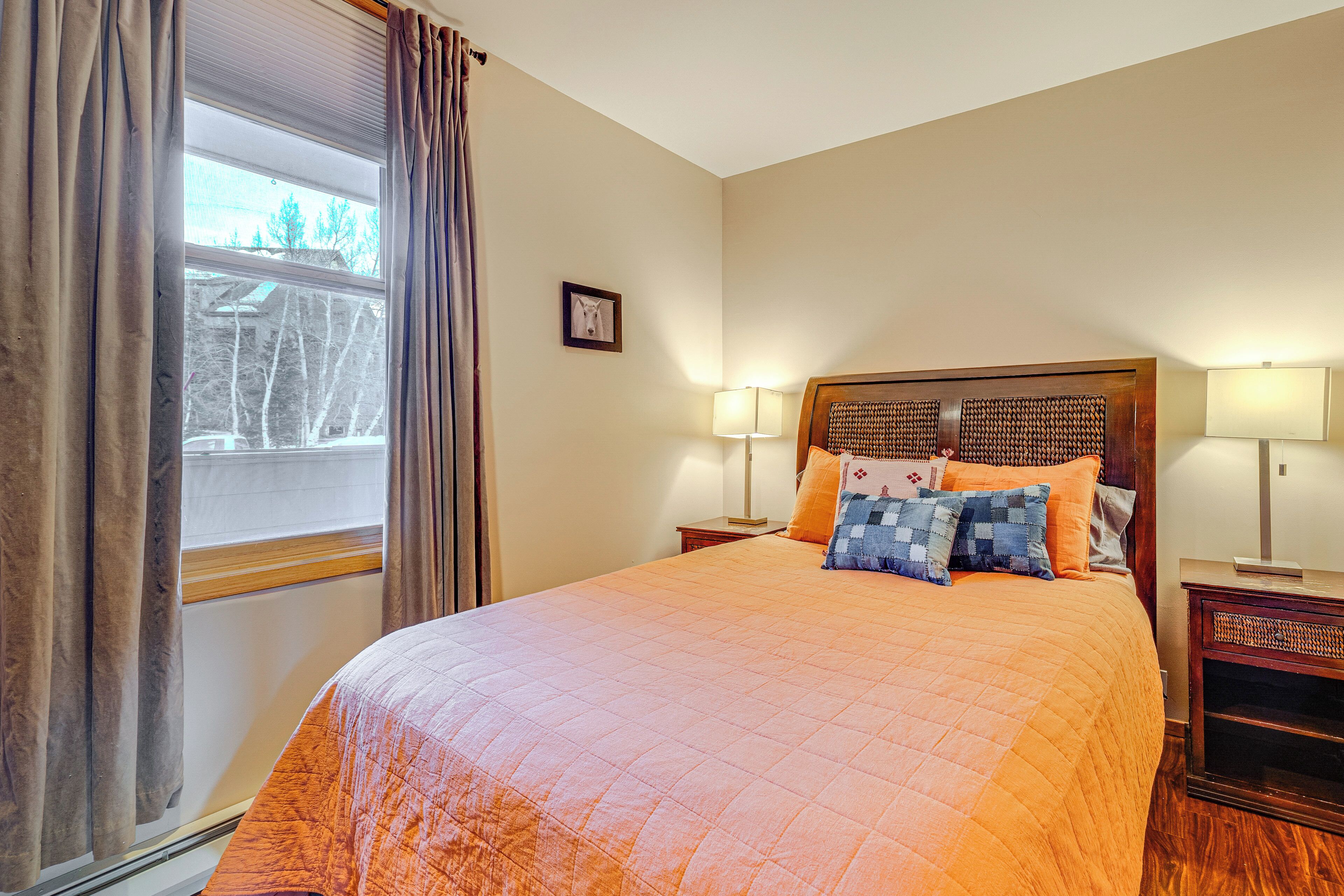 A neatly made bed with an orange quilt, a wooden headboard, and two bedside lamps.
